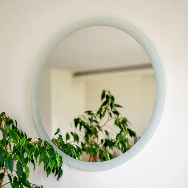 Szlifowana tafla lustra z dekoracyjnym roślinnym tłem, zawieszona przy konsoli z drewnianym blatem. Szlifowane lustro dekoracyjne dostępne w sklepie internetowym Magia Lustra – magialustra.pl.