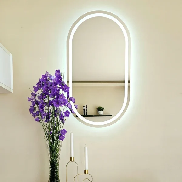 Owalne lustro łazienkowe LED bez ramy, zamontowane na jasnej ścianie z dekoracyjną rośliną. Lustro LED owalne jest dostępne w sklepie internetowym Magia Lustra – magialustra.pl