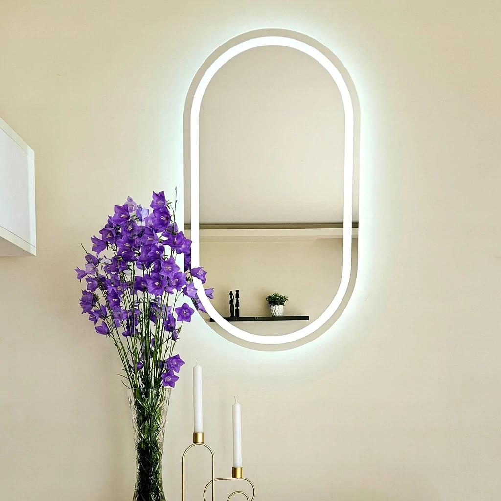 Owalne lustro łazienkowe LED bez ramy, zamontowane na jasnej ścianie z dekoracyjną rośliną. Lustro LED owalne jest dostępne w sklepie internetowym Magia Lustra – magialustra.pl