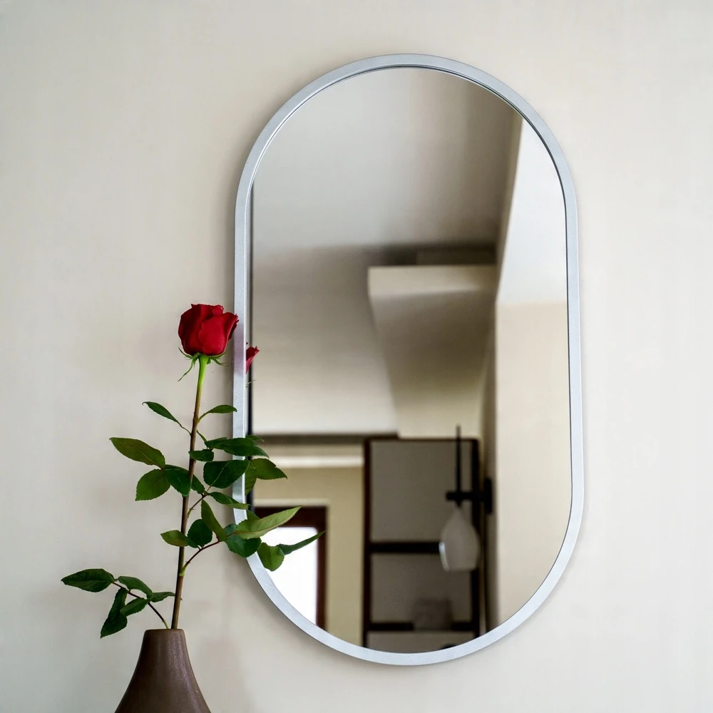 Owalne lustro w srebrnej ramie, zawieszone nad umywalką w eleganckiej łazience. Lustro w srebrnej ramie jest dostępne w sklepie internetowym Magia Lustra – magialustra.pl.